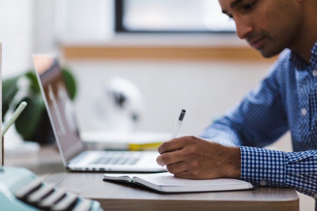 jeune homme qui prend des notes devant son ordinateur